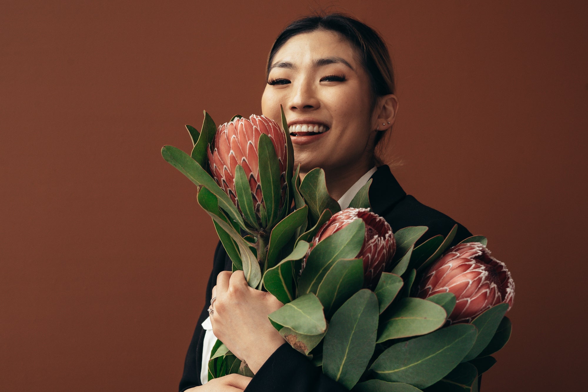 Person wearing a suit jacket smiles and hugs a bouquet of large flowers