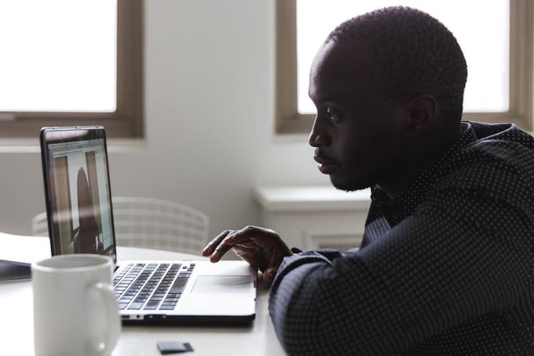 App store lessons: Photo of a man sitting at his laptop on a video call. His profile is illuminated by the bright windows behind him and has a cup of coffee on his desk on his left side.