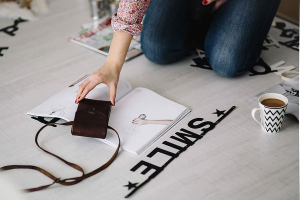 Mulher trabalhando no chão em minibolsa com revista ao seu redor e letras espalhadas pelo ambiente