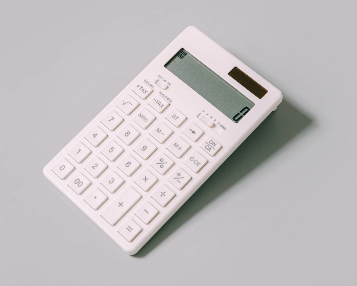 Das Foto zeigt einen weißen Taschenrechner auf grauem Hintergrund. Mit dem Taschenrechner lassen sich Konten durchkalkulieren, die du dir zuvor im Geschäftskonto-Vergleich angeschaut hast.